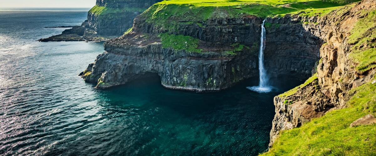 A coastal landscape with a waterfall, green cliffs, and a village.