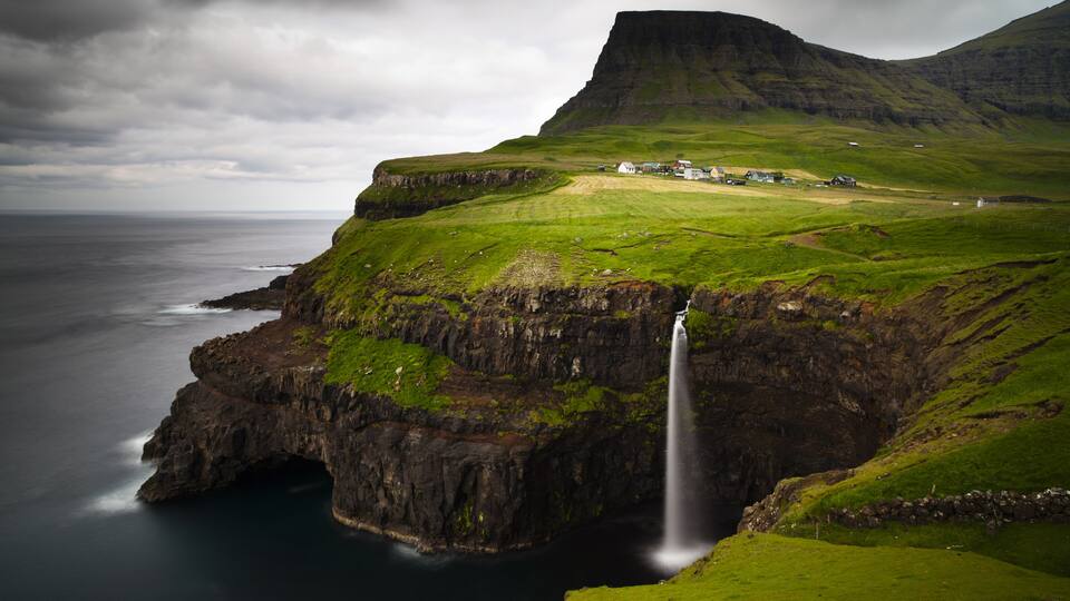 A coastal landscape with a waterfall, green hills, and a small settlement.