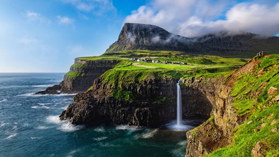 A coastal landscape with a waterfall, green cliffs, and a village.