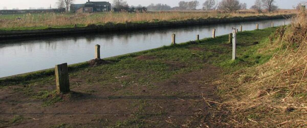 A calm river with a grassy bank, a wooden post, and a distant building.