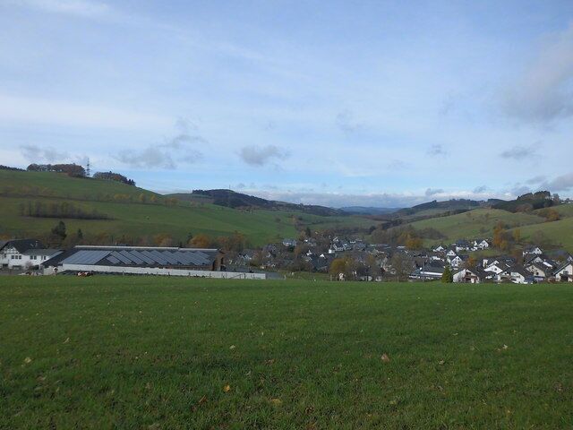 A rural landscape with green fields, a large barn, and a small village with houses.