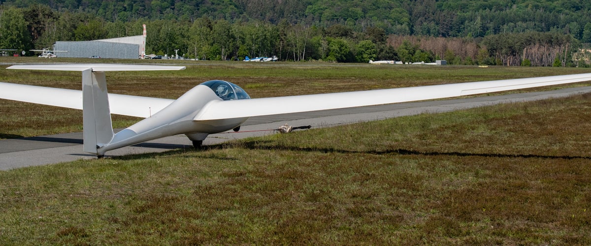 A small white aircraft on a grassy airstrip with a forested hill in the background.