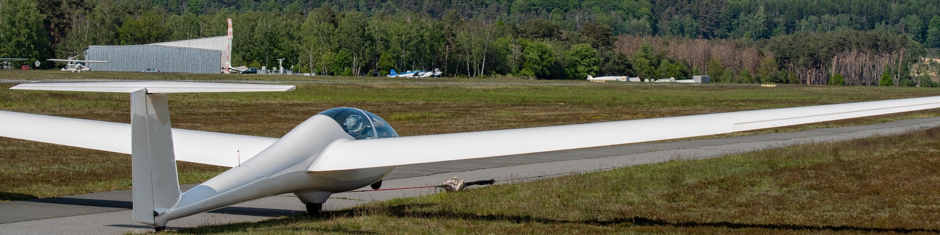A small white aircraft on a grassy airstrip with a forested hill in the background.