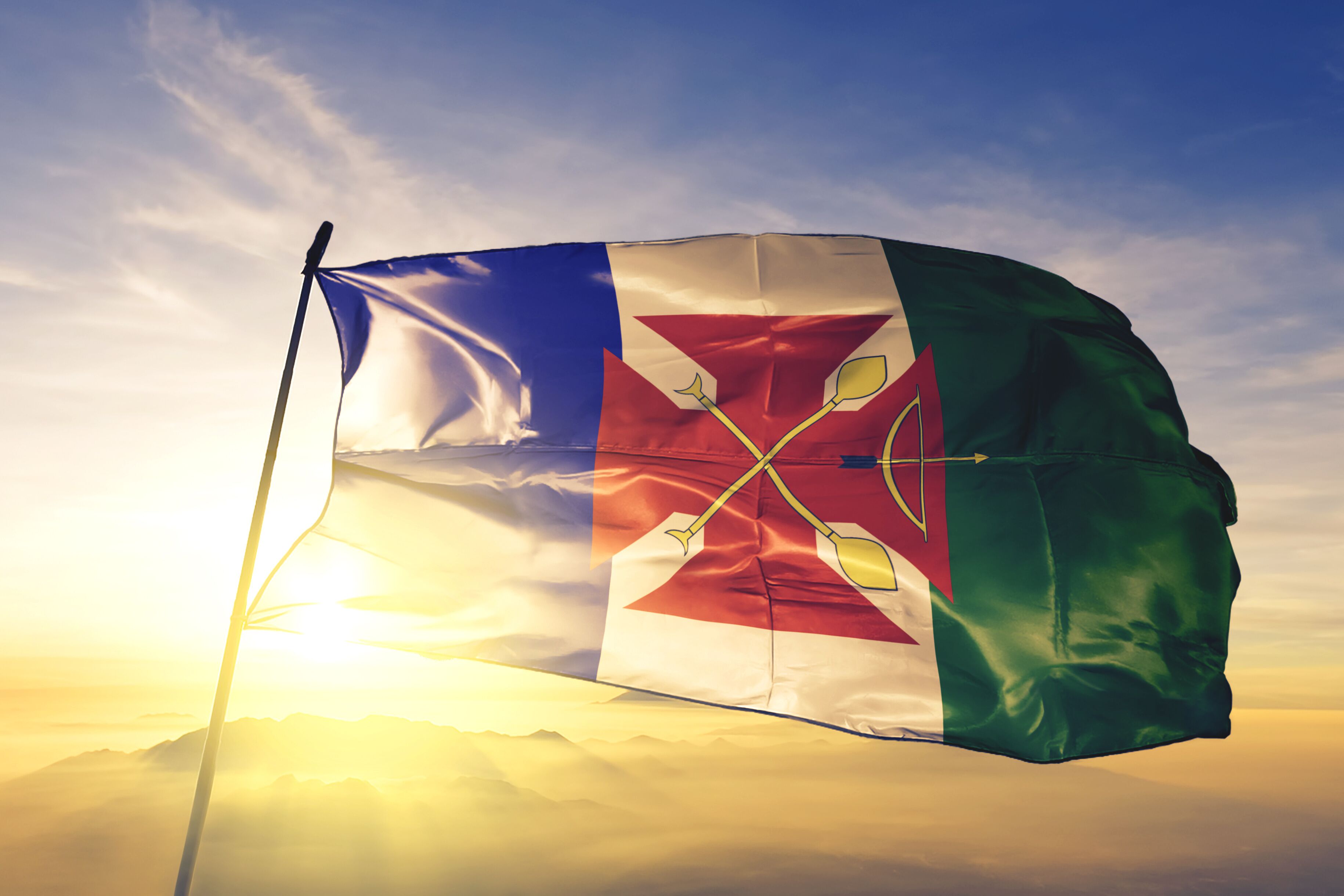 A flag with a red star and two arrows, set against a sunrise or sunset sky.