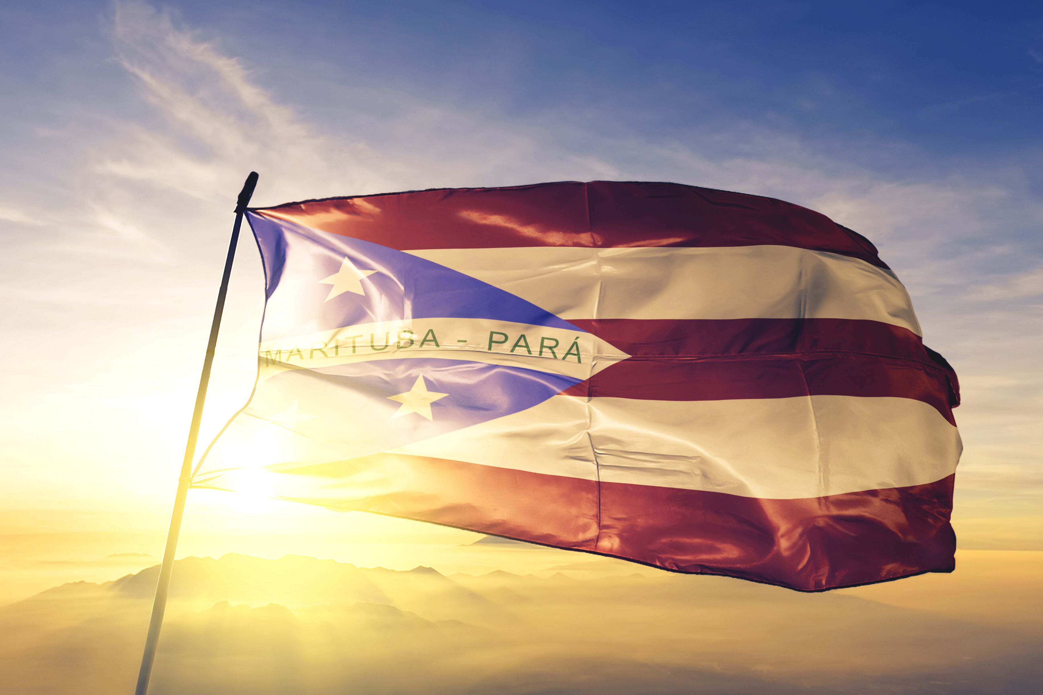 A flag with a banner reading "VENEZUELA - PARA" against a backdrop of a sunrise or sunset over mountains.
