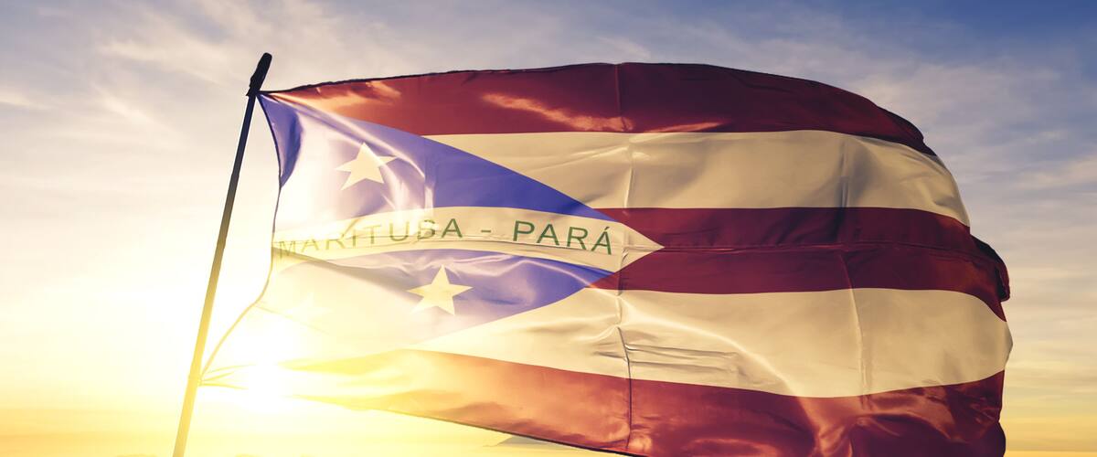 A flag with a banner reading "VENEZUELA - PARA" against a backdrop of a sunrise or sunset over mountains.