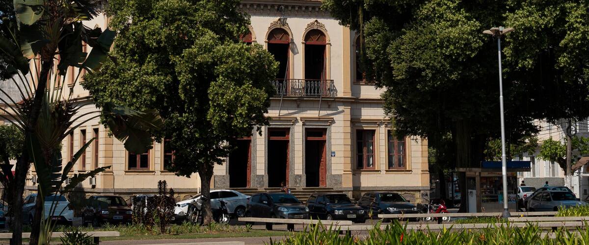A historic building with a clock tower, surrounded by lush greenery and parked cars.