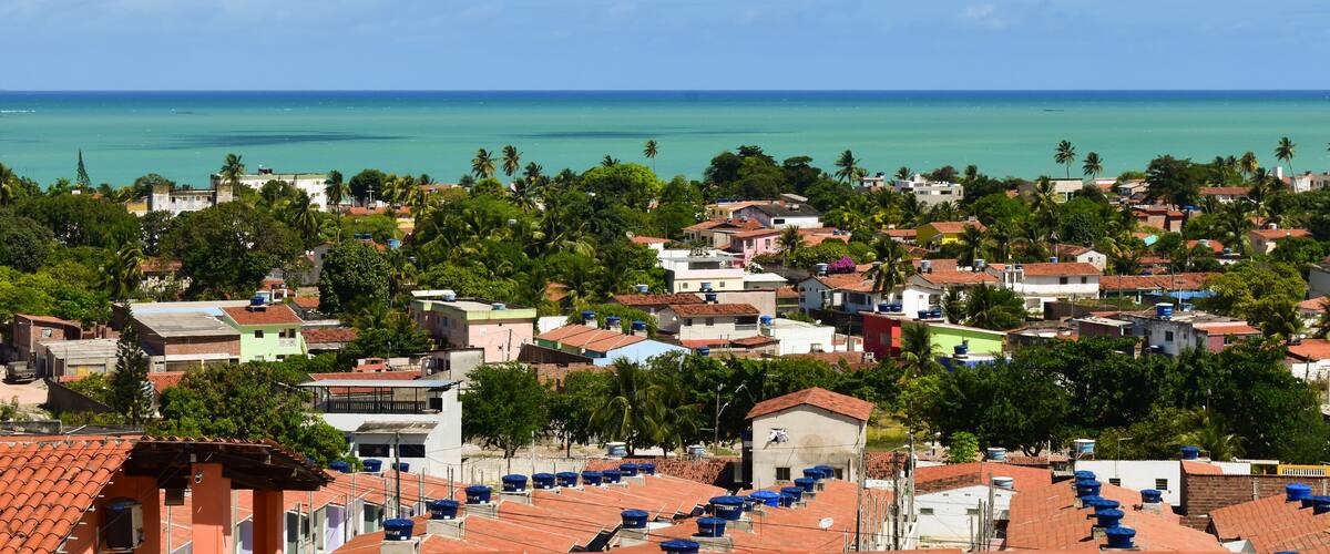 A coastal town with terracotta-roofed buildings, palm trees, and a clear view of the ocean.