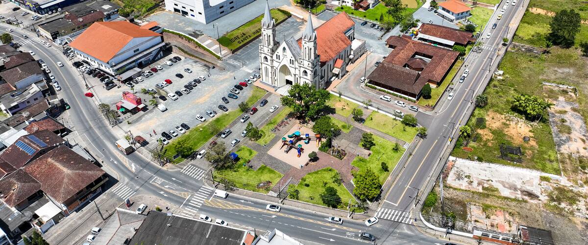 An aerial view of a town with a prominent church, a parking lot, and surrounding greenery.