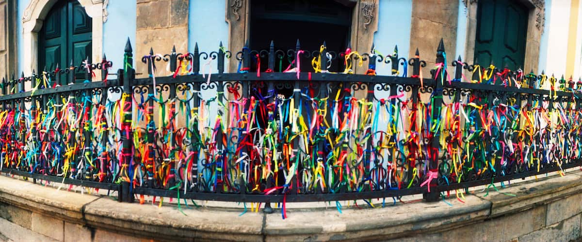 A black wrought iron fence with colorful ribbons tied to its spikes.