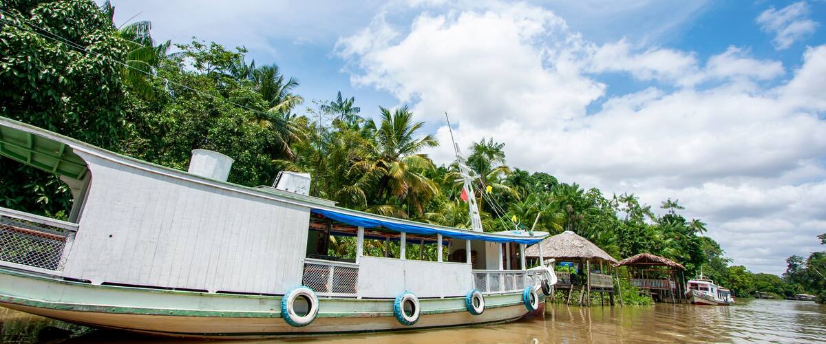 A boat docked in a river surrounded by lush greenery and a thatched-roof hut.