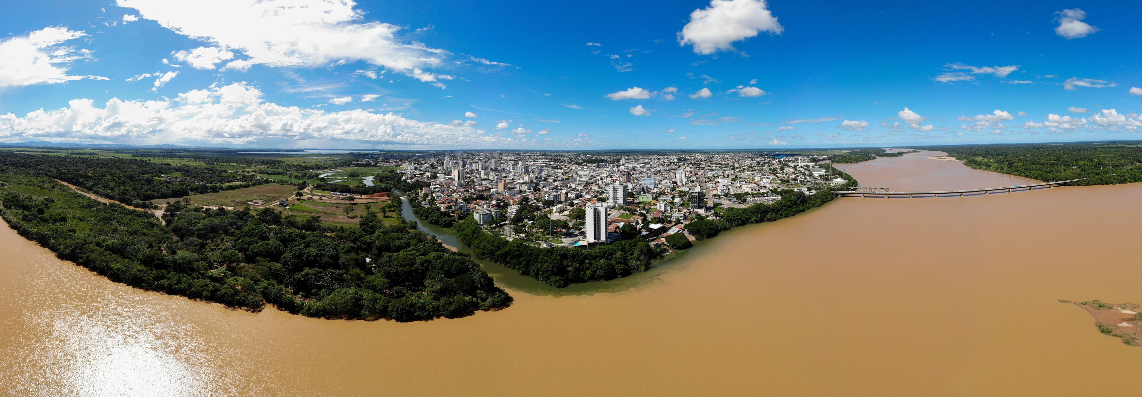 An aerial view of a city with a river, green areas, and a bridge.