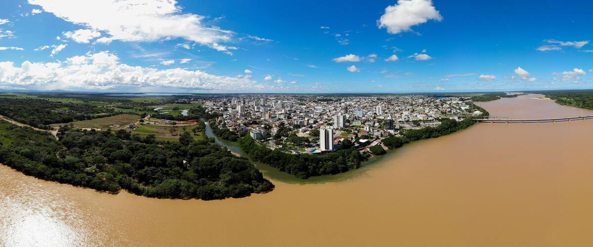 An aerial view of a city with a river, green areas, and a bridge.