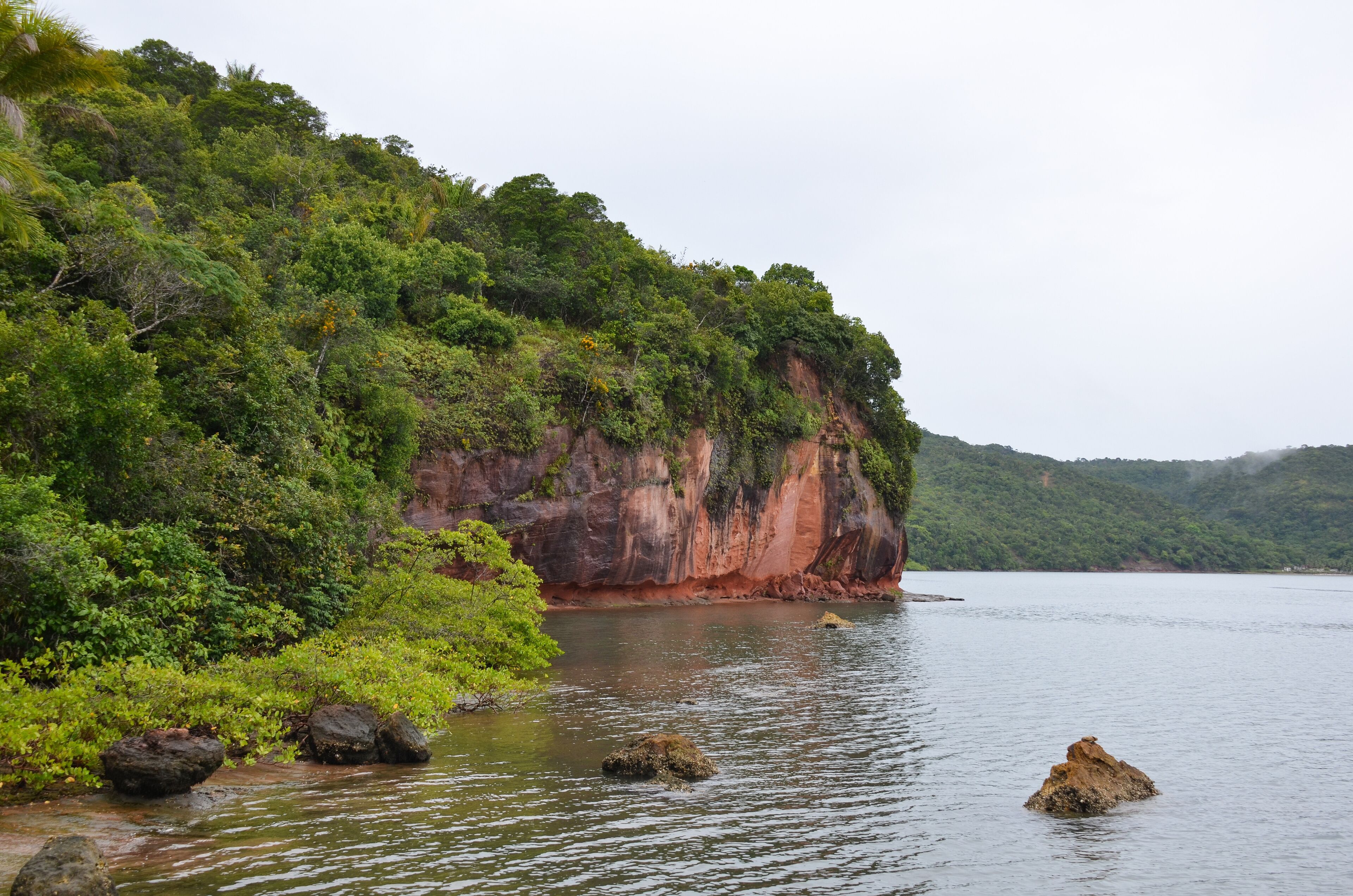 A calm lake surrounded by lush green hills and a prominent red cliff.