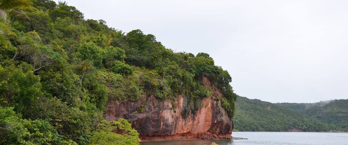 A calm lake surrounded by lush green hills and a prominent red cliff.
