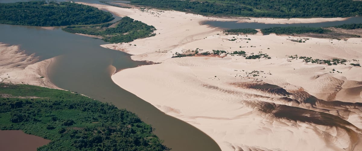 A river winding through a desert landscape with sand dunes and green vegetation.