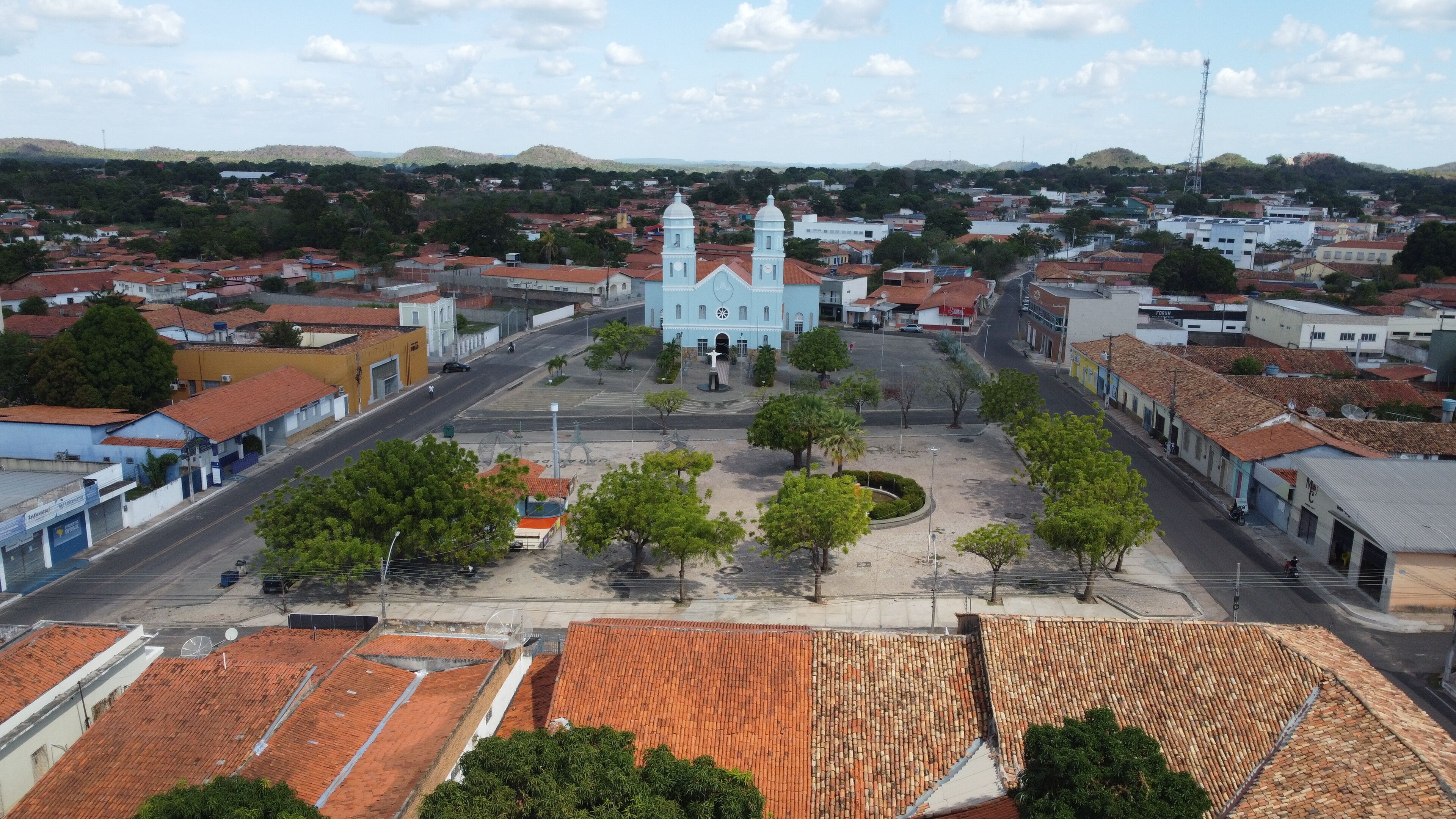 A town square with a prominent church, surrounded by residential buildings and hills in the background.