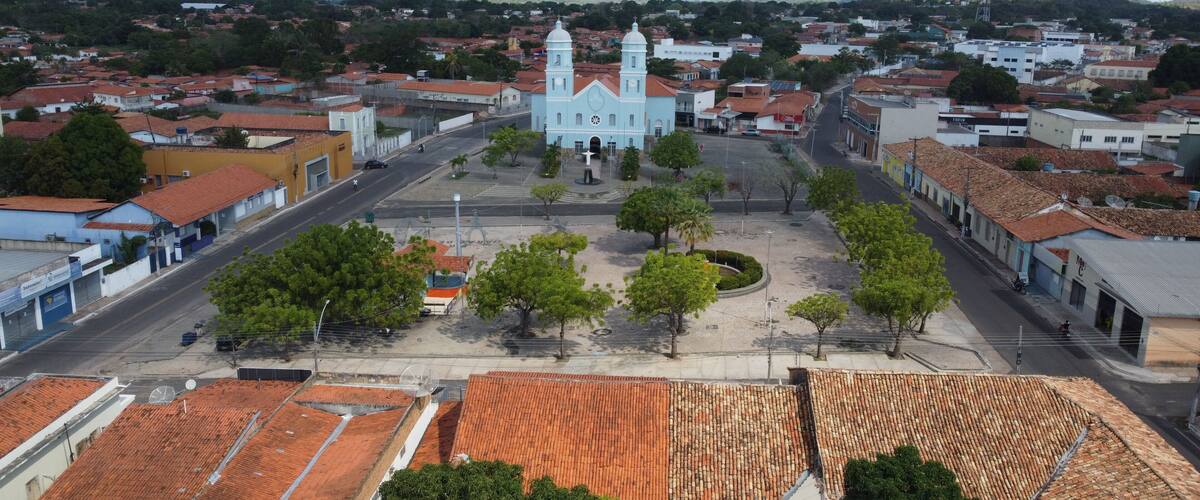 A town square with a prominent church, surrounded by residential buildings and hills in the background.