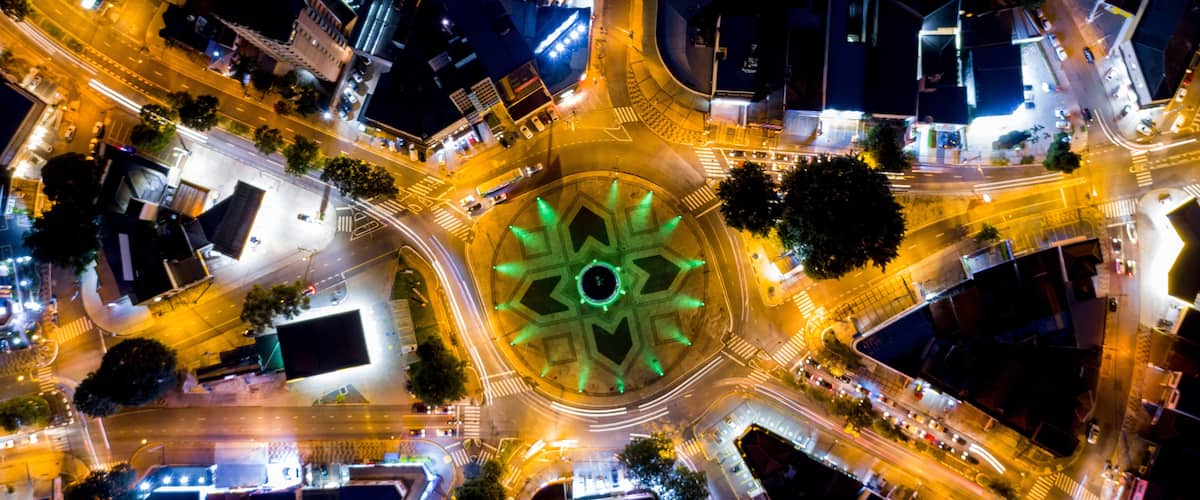 An aerial view of a roundabout with a central green decorative structure, surrounded by intersecting roads and buildings.
