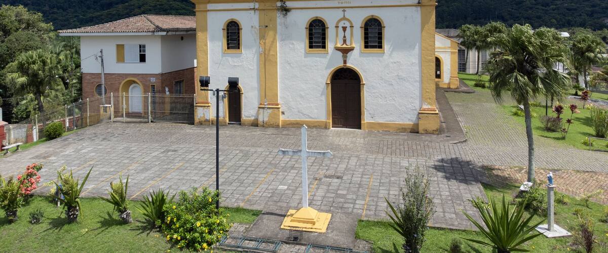 A historic church with a bell tower and a clock, surrounded by a paved courtyard and lush greenery.