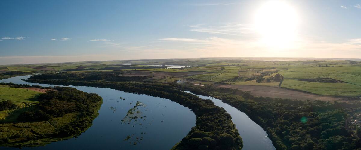 A river winding through a green landscape with fields and a distant body of water.
