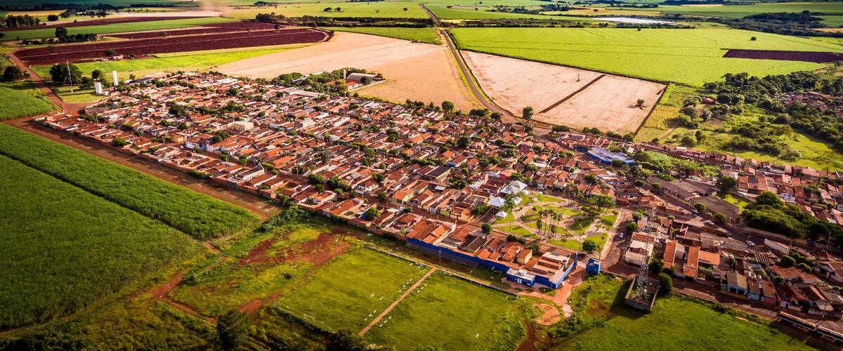 An aerial view of a town with a grid of houses, surrounded by green fields and a large open area.