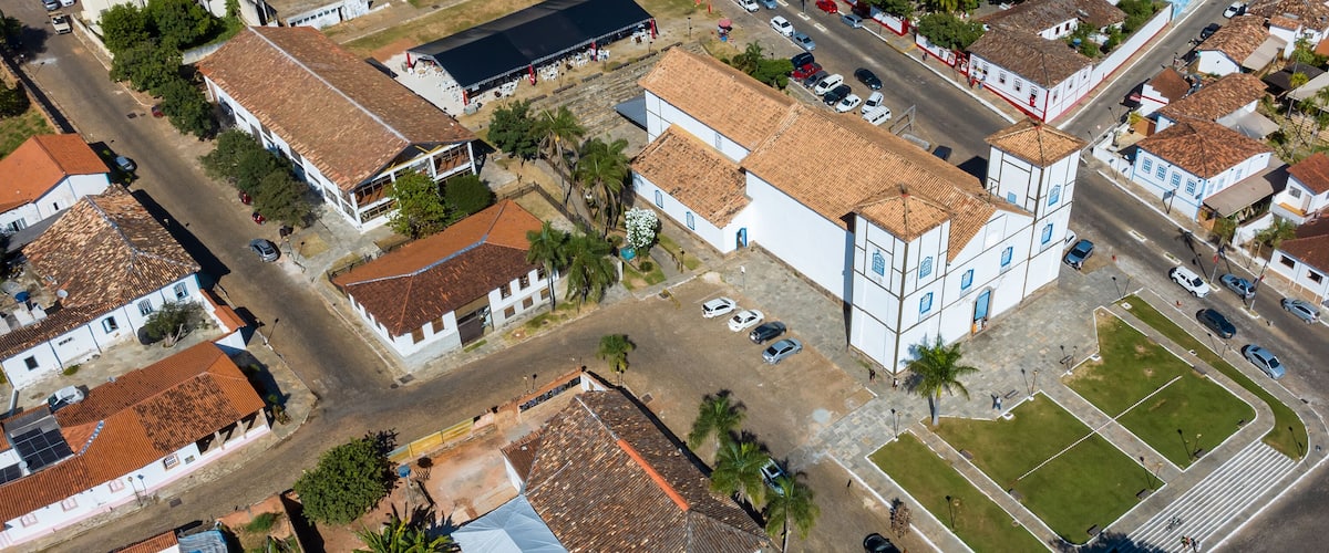An aerial view of a residential area with white buildings, red-tiled roofs, and a central open space with a fountain.