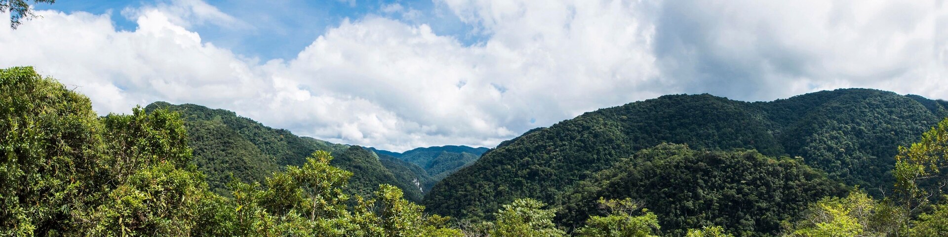 Paisagem com o verde da Mata Atlântica na parte inferior e o azul do céu e o branco das nuvens na parte superior do quadro. Vale do Ribeira, São Paulo, Brasil.