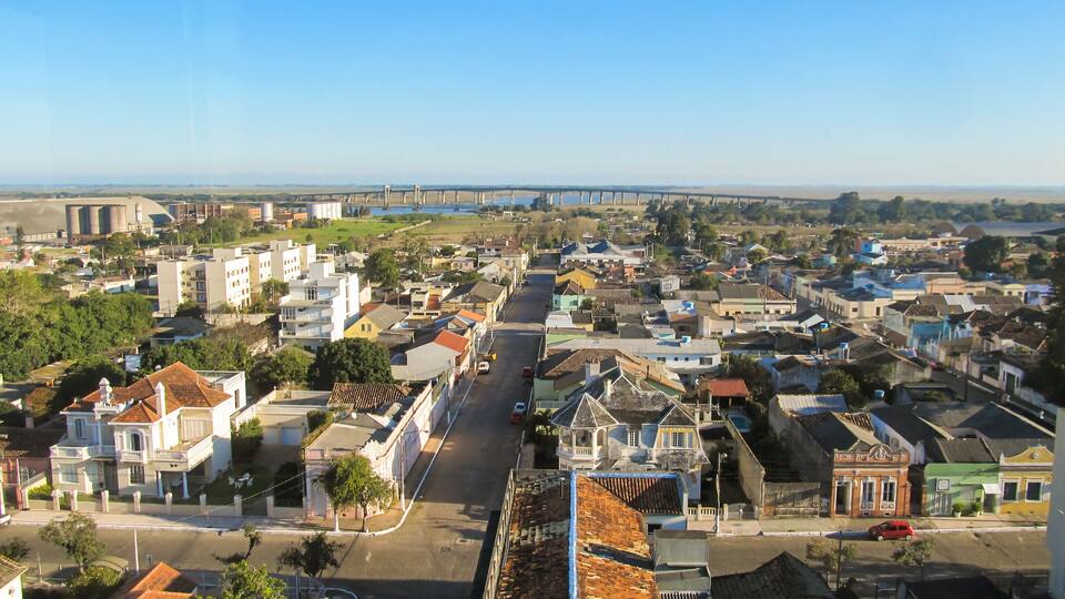 A coastal cityscape with a prominent bridge in the distance, colorful buildings, and a clear sky.
