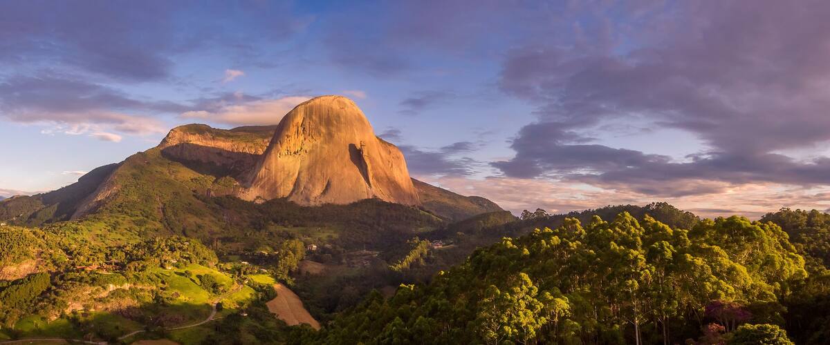 A mountain with a prominent peak, surrounded by lush green forests and rolling hills.