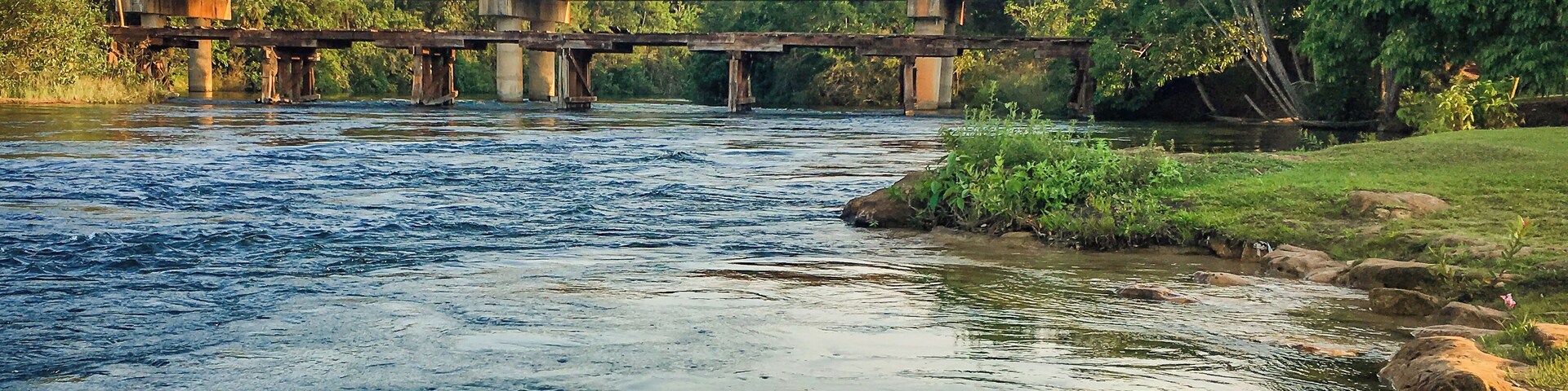 A river with a bridge, rocks, and greenery.