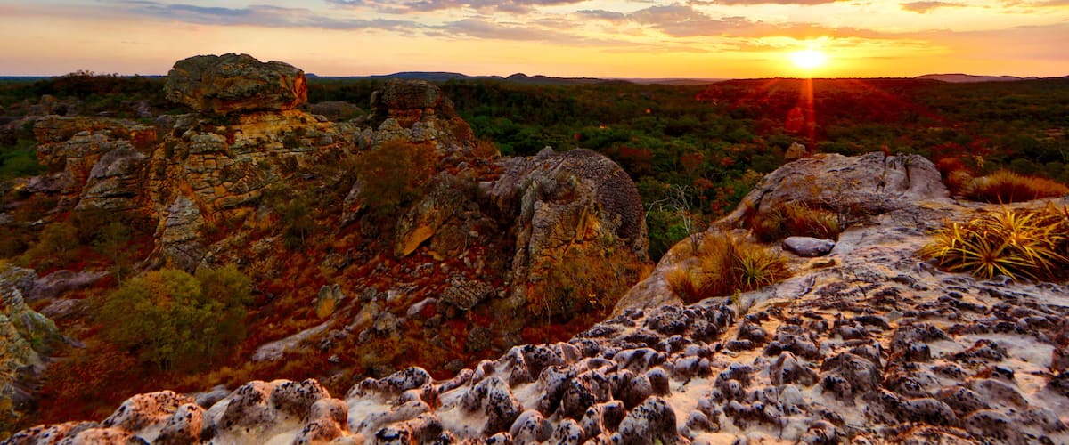 A sunset over a rocky landscape with prominent rock formations and sparse vegetation.