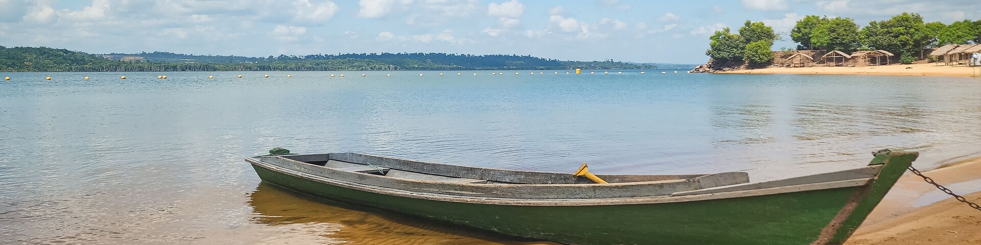 Un bote verde en una playa arenosa, con agua tranquila y un cielo despejado.