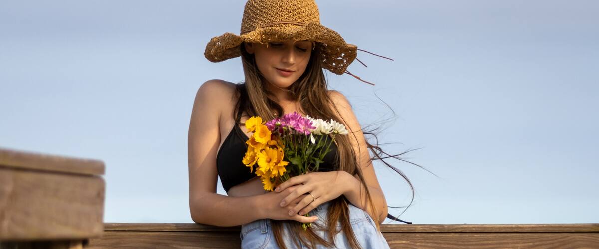 A person standing on a wooden boardwalk by the ocean, holding a bouquet of flowers.