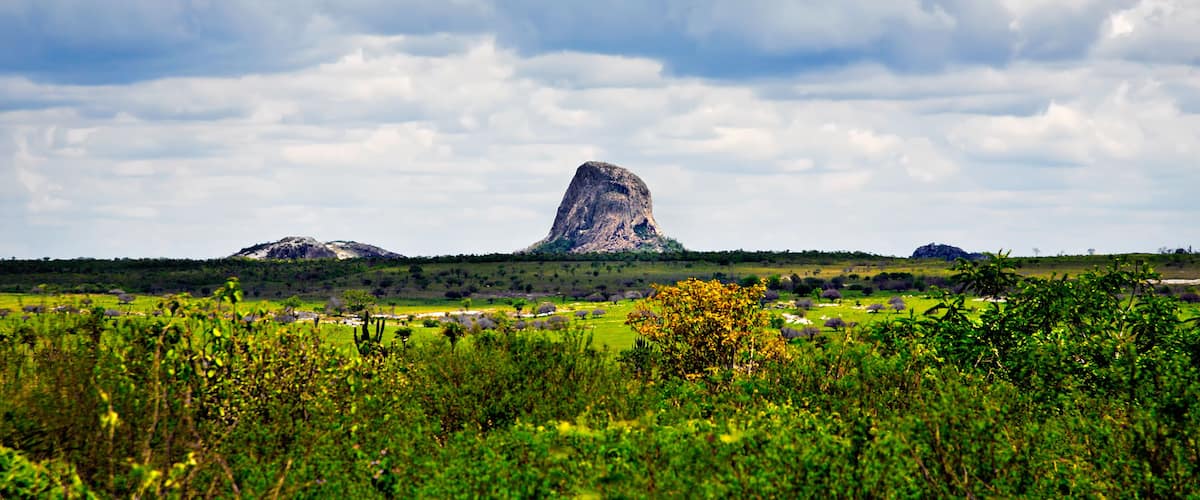 A landscape with a prominent rock formation in the center, surrounded by green fields and scattered trees.