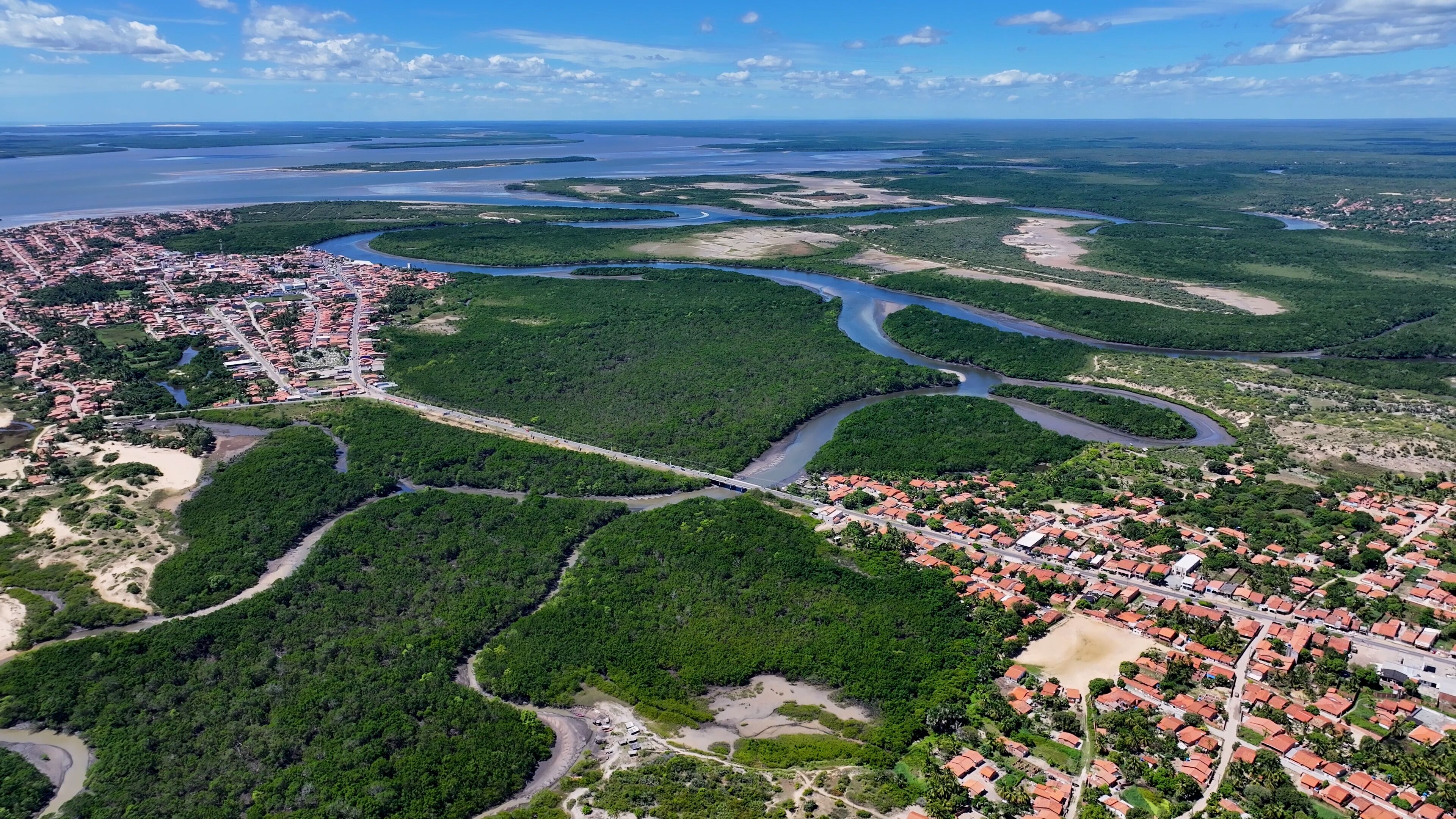 An aerial view of a coastal city with dense green areas, winding rivers, and a bridge connecting two parts of the city.