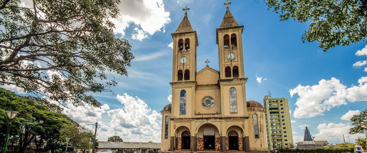 A church with two towers and a clock, surrounded by a paved area and greenery.