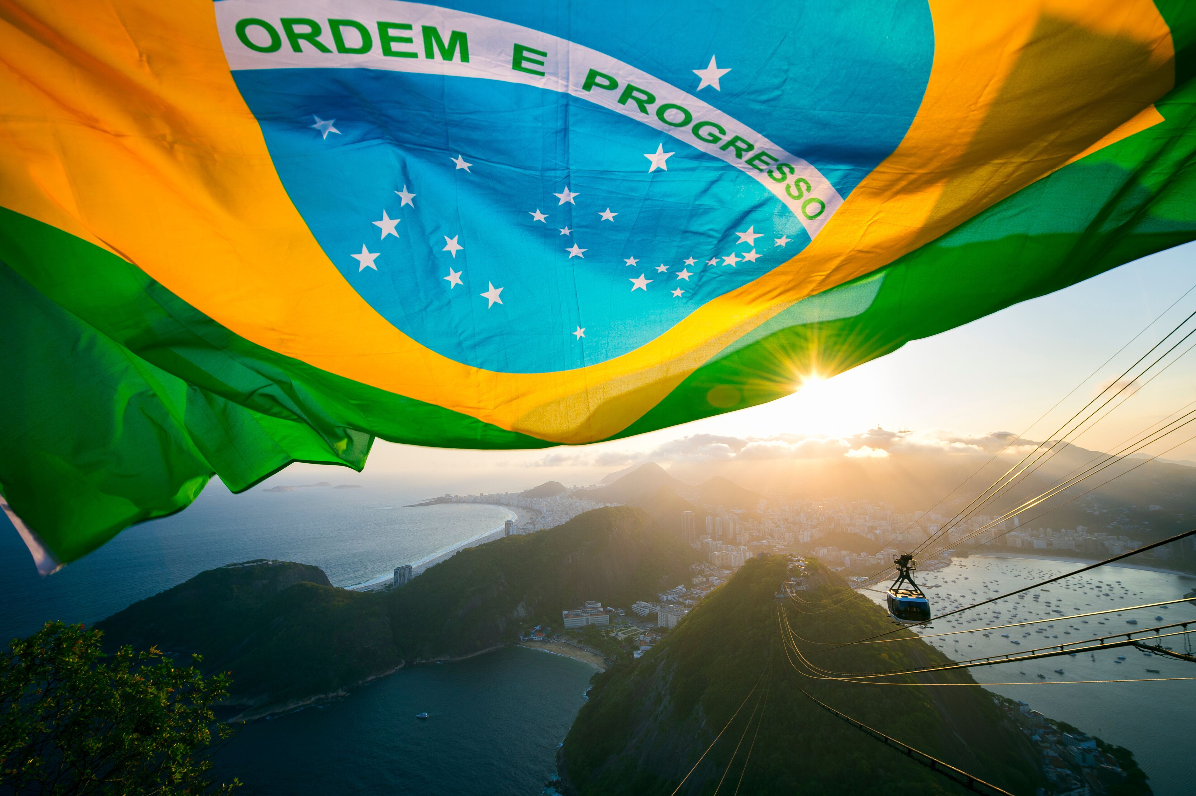 Brazilian flag shines above the golden sunset city skyline at Sugarloaf Pao de Acucar Mountain in Rio de Janeiro Brazil