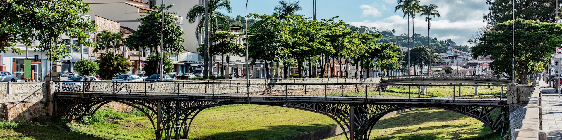 Un puente sobre una zona cubierta de césped, con palmeras y edificios al fondo.