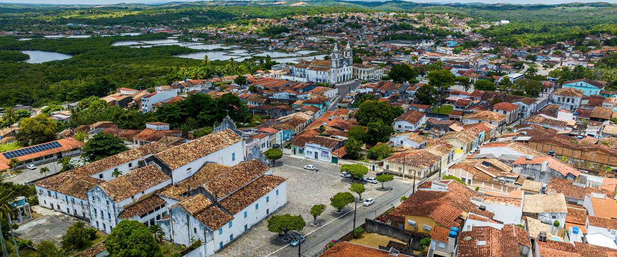 An aerial view of a historic town with terracotta-roofed buildings, a prominent church, and surrounding greenery.