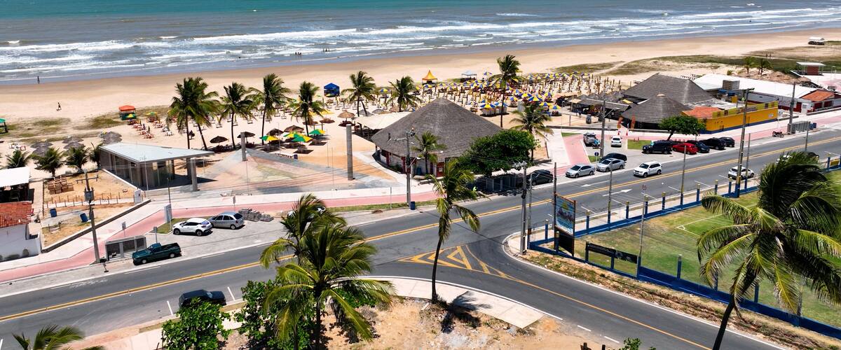 Un pueblo frente al mar con una carretera, palmeras, sombrillas de playa y vistas al océano.