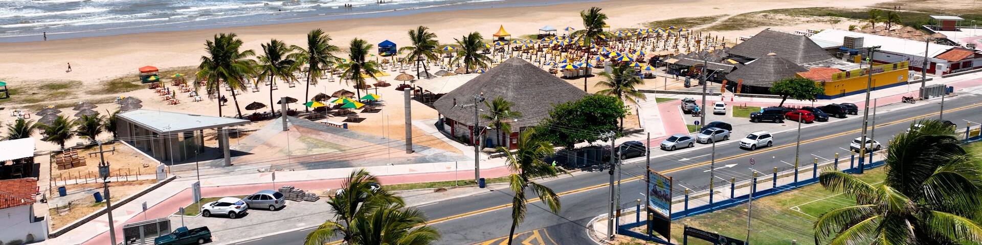 A beachside town with a road, palm trees, beach umbrellas, and a view of the ocean.