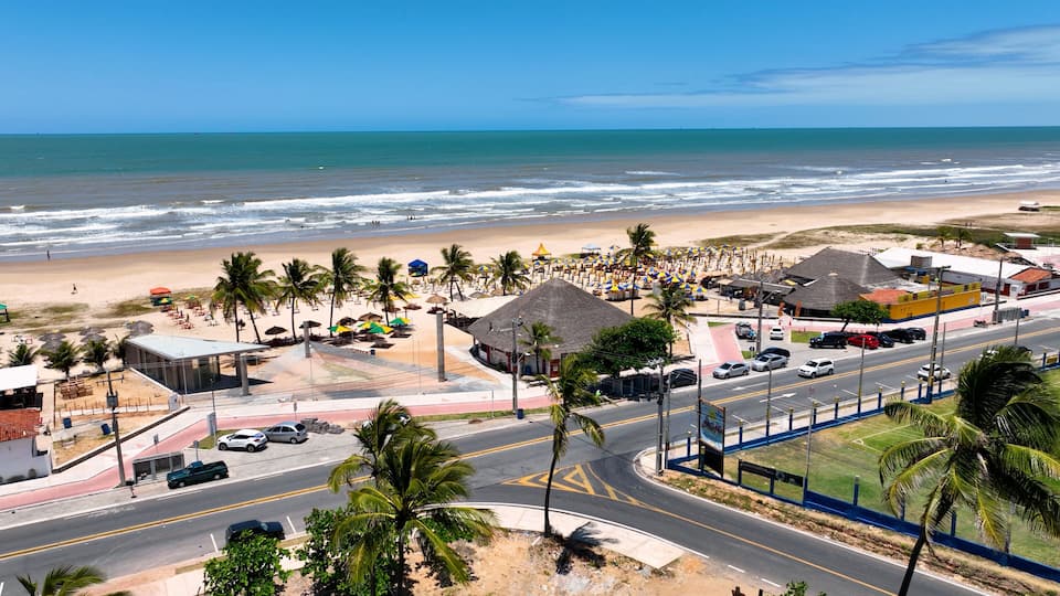 A beachside town with a road, palm trees, beach umbrellas, and a view of the ocean.