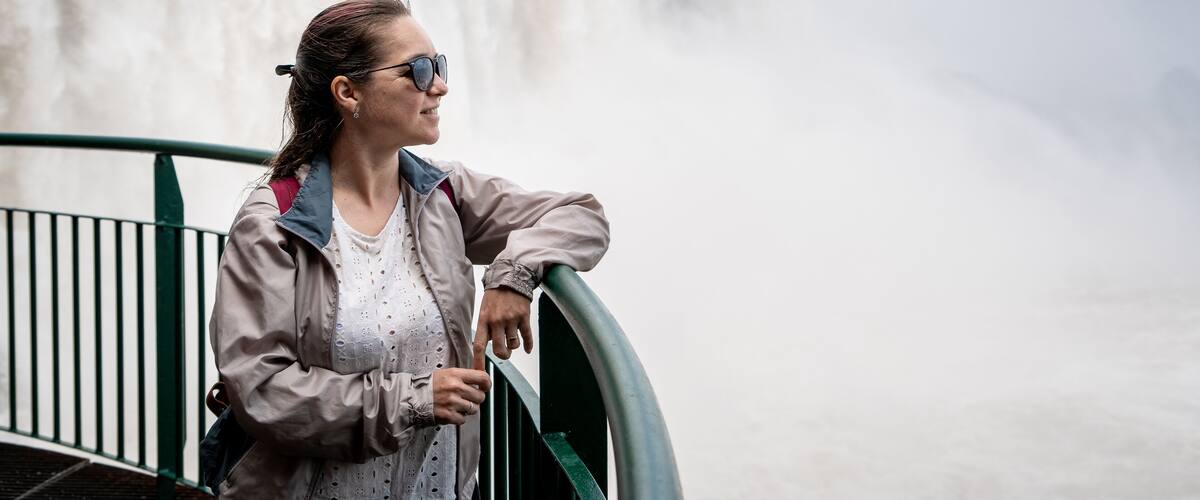 A person leaning on a railing with a waterfall in the background.