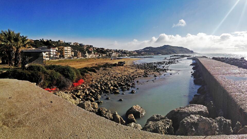 A coastal landscape with a rocky shoreline, a beach, and a residential area in the background.