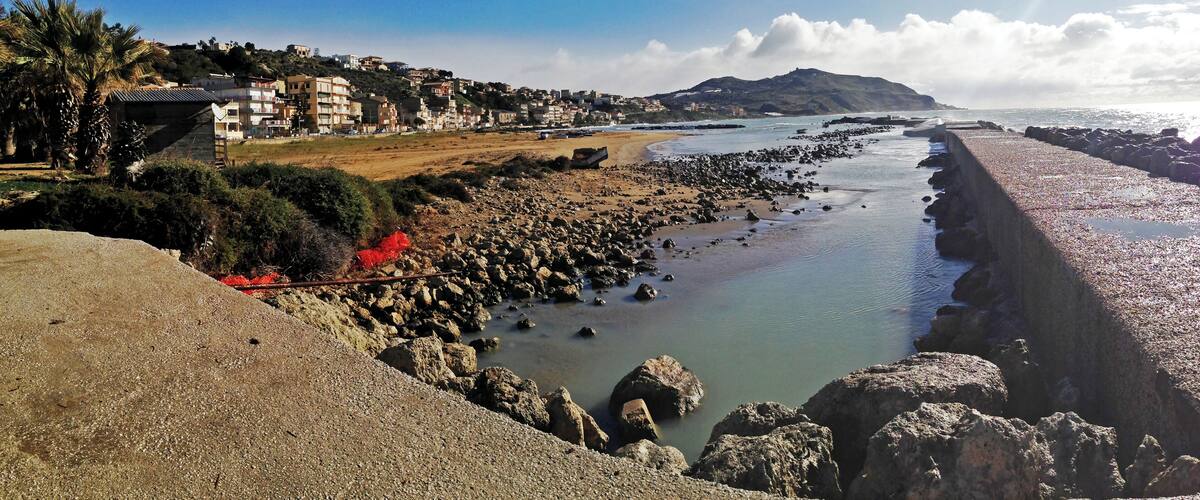 A coastal landscape with a rocky shoreline, a beach, and a residential area in the background.