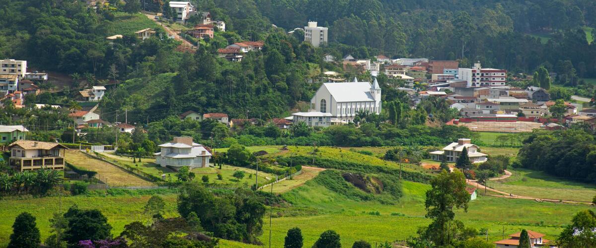 A lush green hillside town with a prominent white church, surrounded by mountains.