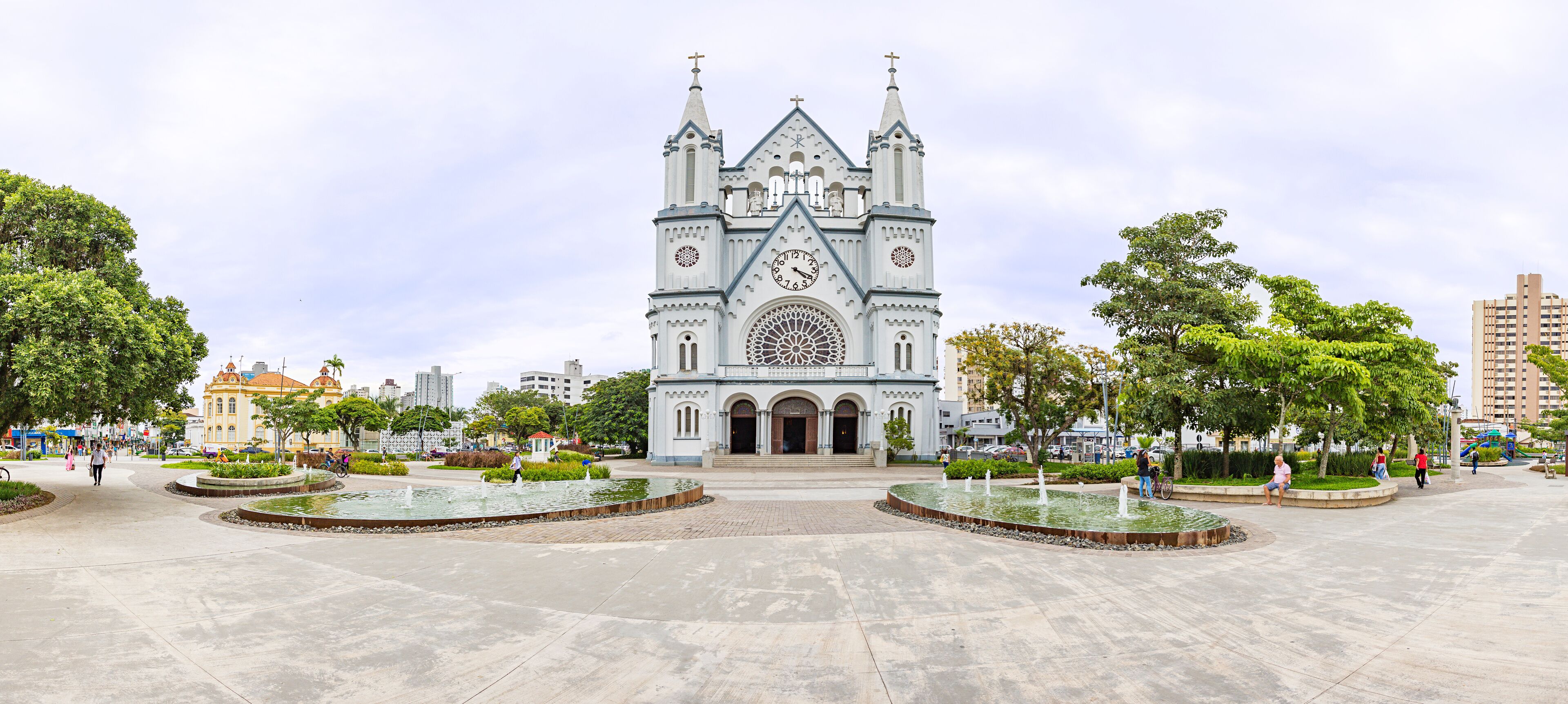 A large cathedral with a clock tower and a circular fountain in the plaza.
