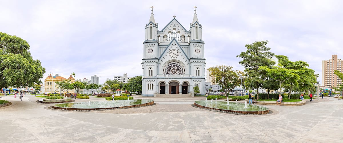 A large cathedral with a clock tower and a circular fountain in the plaza.