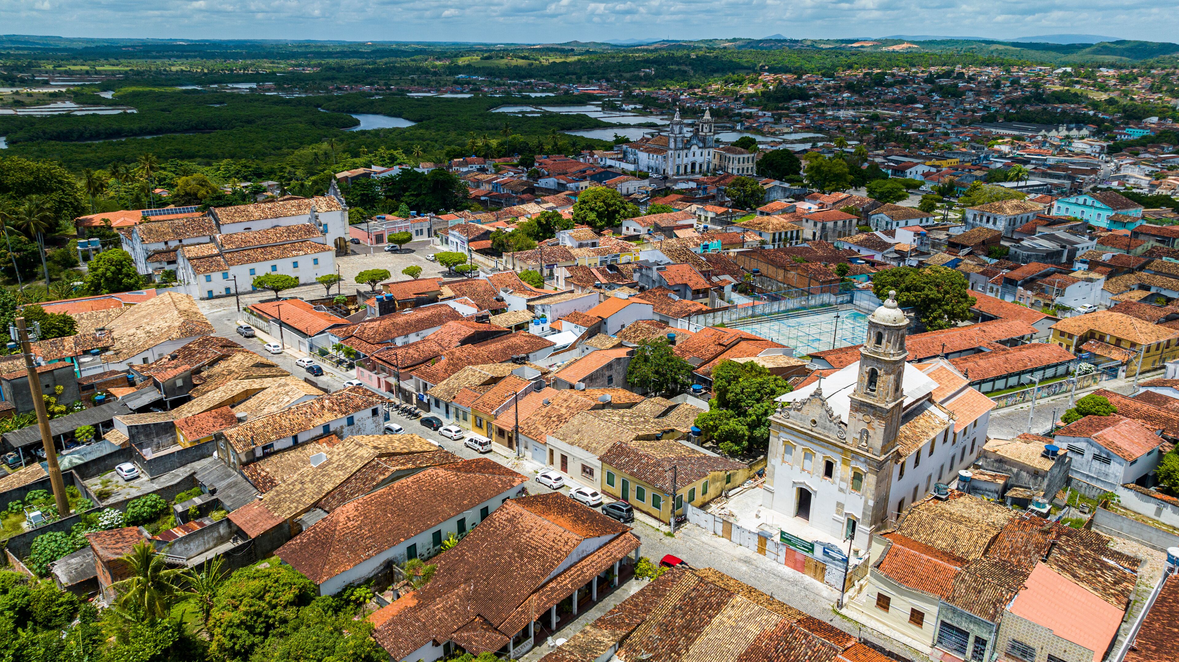 A historic town with terracotta-roofed buildings, a prominent church, and a river in the background.